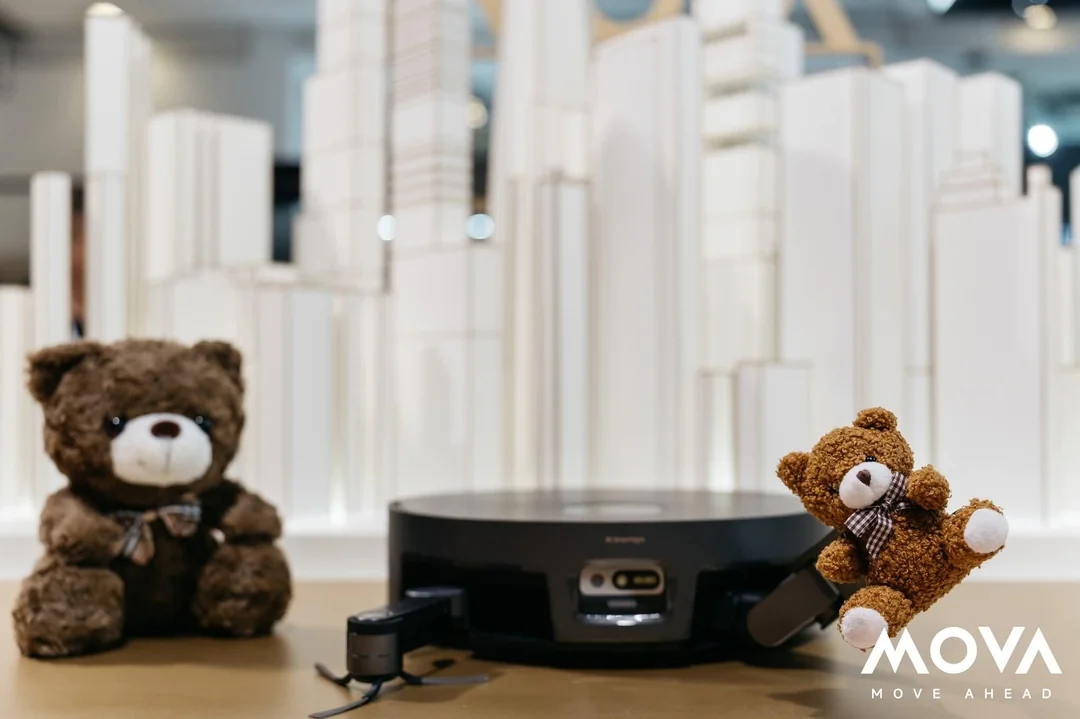 MOVA Sirius 60 with it's side brush extended in one arm and another arm holding a toy bear.